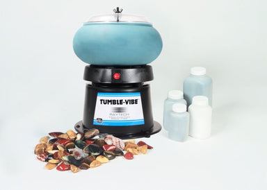 Close up of vibratory tumbler with blue noise reducing bowl, 4 piece grit set and rocks placed decoratively in front of the bowl.