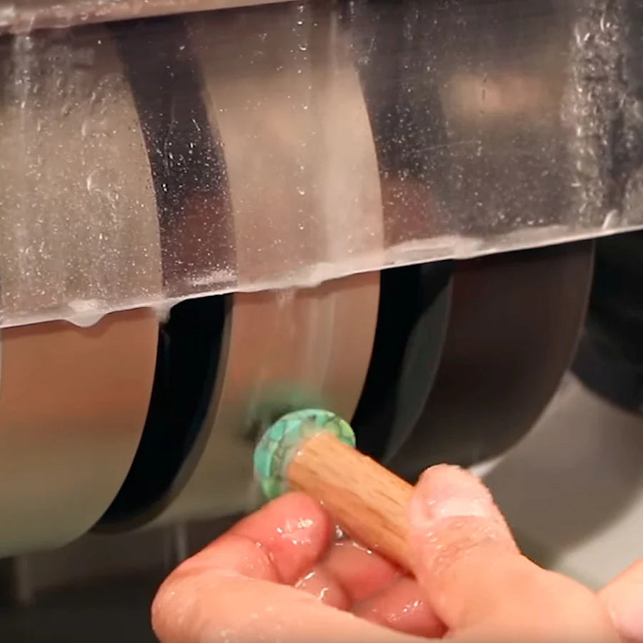 close up of hands holding a green gemstone on a wet spinning, grinding diamond wheel on the cabking 6 cabbing machine with water dripping from stone