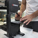 person holding a stone on the top surface and using the rock cutting bandsaw, the db-100 wet band saw and cutting through it 