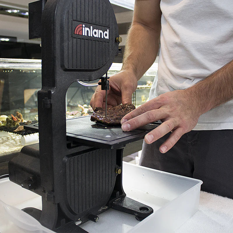 person holding a stone on the top surface and using the rock cutting bandsaw, the db-100 wet band saw and cutting through it 