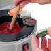 close up of hands holding a lapidary dop stick in melted wax in a dop pot while holding a gemstone