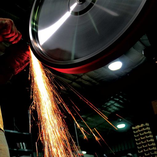 man grinding metal on burr king bba20 20" belt grinder with lots of sparks shootting to the ground