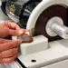 man holding a rock or gemstone to the cabking cabbing machine trim saw attachement and slicing the rock in half with  a water drip to cool the rock and prevent overheating