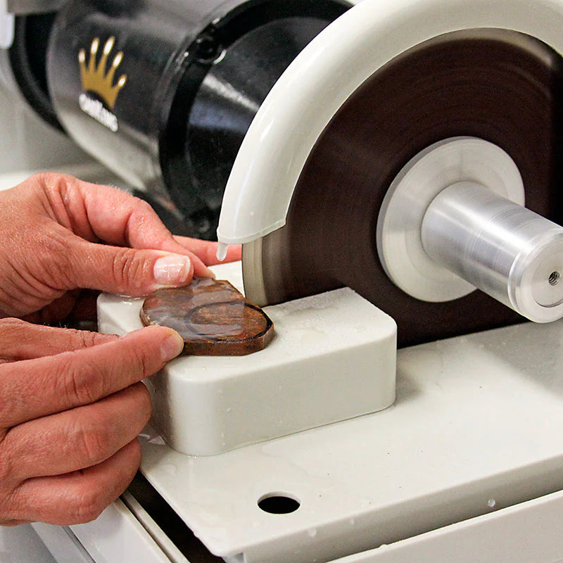 man holding a rock or gemstone to the cabking cabbing machine trim saw attachement and slicing the rock in half with  a water drip to cool the rock and prevent overheating