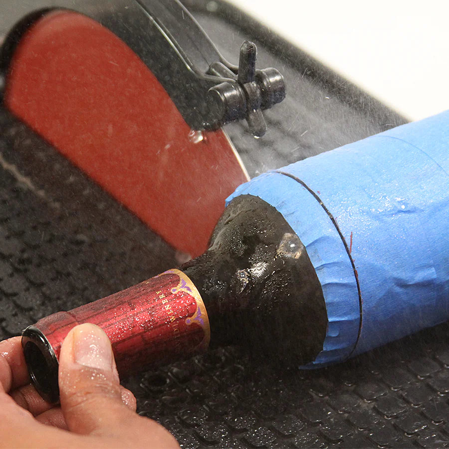 close up of hands cutting a wine bottle with the hi tech saw with spinning red blade and water drip on with water splashing